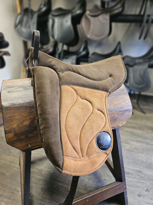 A brown bareback pad designed for horses, displayed in a store with various equestrian equipment in the background.